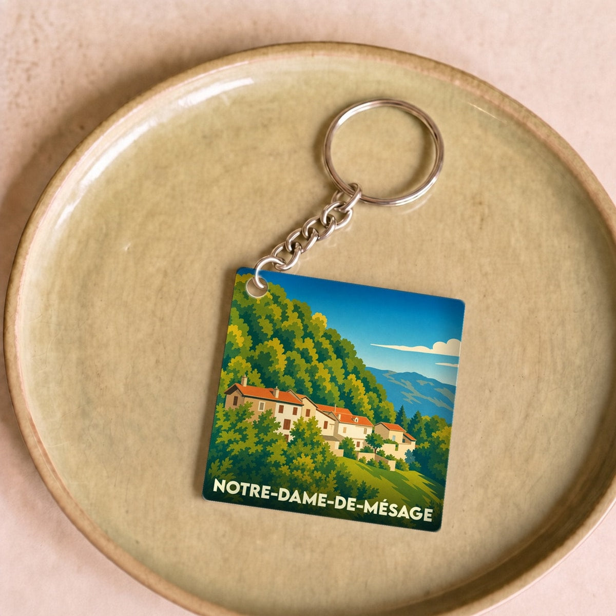 Porte-clés souvenir de Notre-Dame-de-Mésage avec une illustration stylisée du village et de sa montagne boisée.