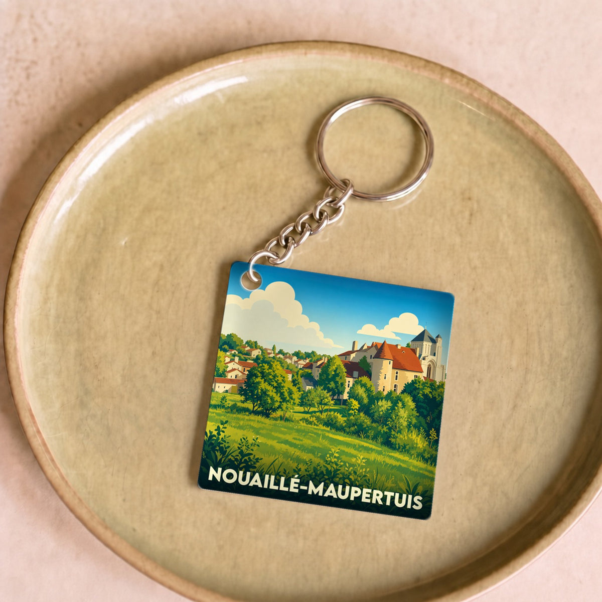 Porte-clés souvenir de la ville de Nouaillé-Maupertuis avec une illustration paysagère stylisée.