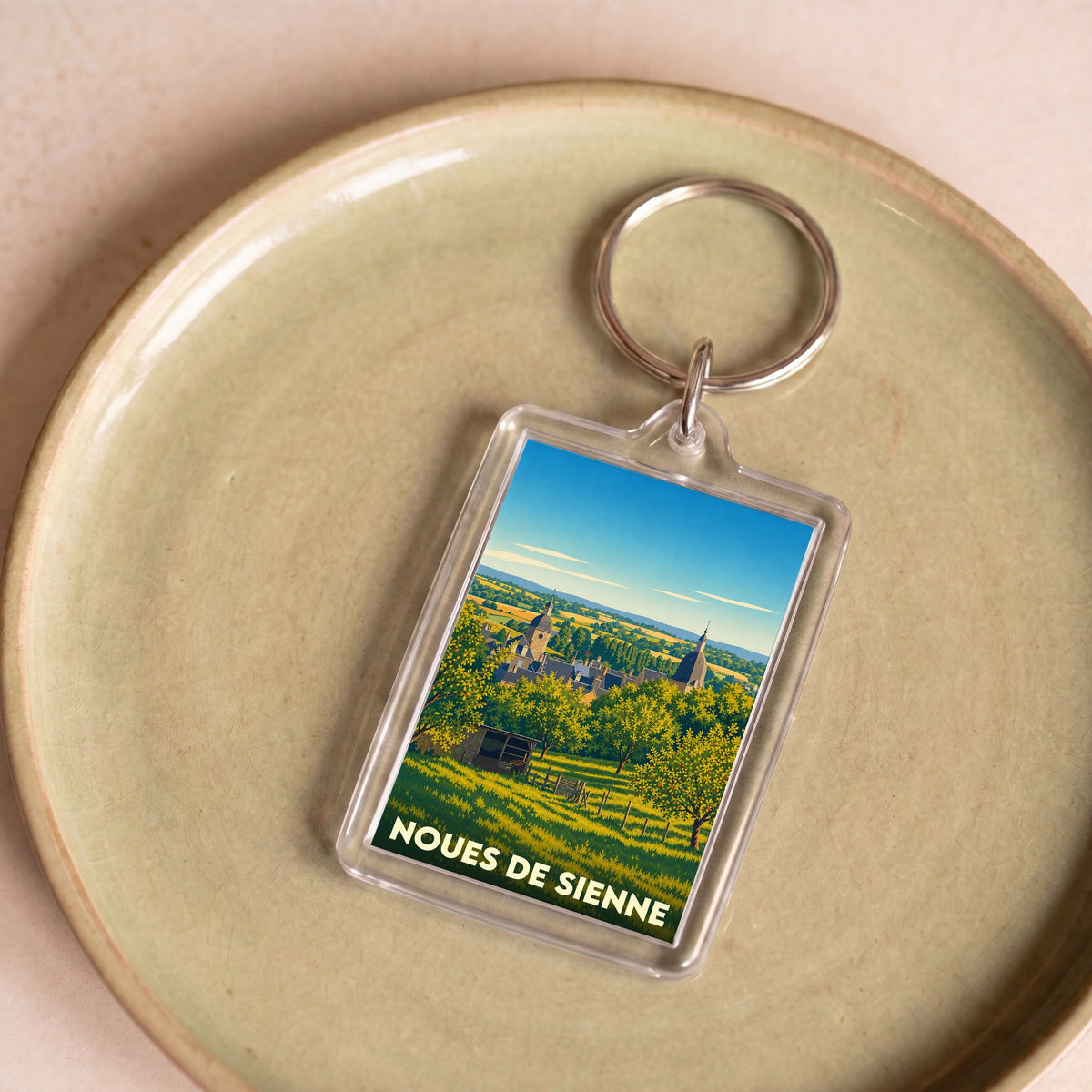 Porte-clés souvenir de la commune de Noues de Sienne avec une illustration paysagère stylisée.