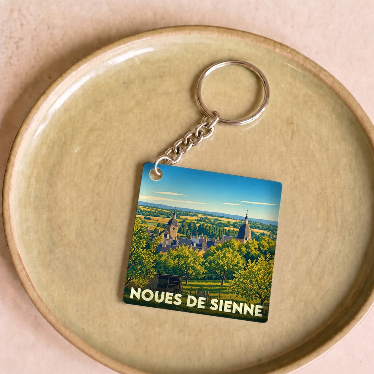 Porte-clés souvenir de la commune de Noues de Sienne avec une illustration paysagère stylisée.