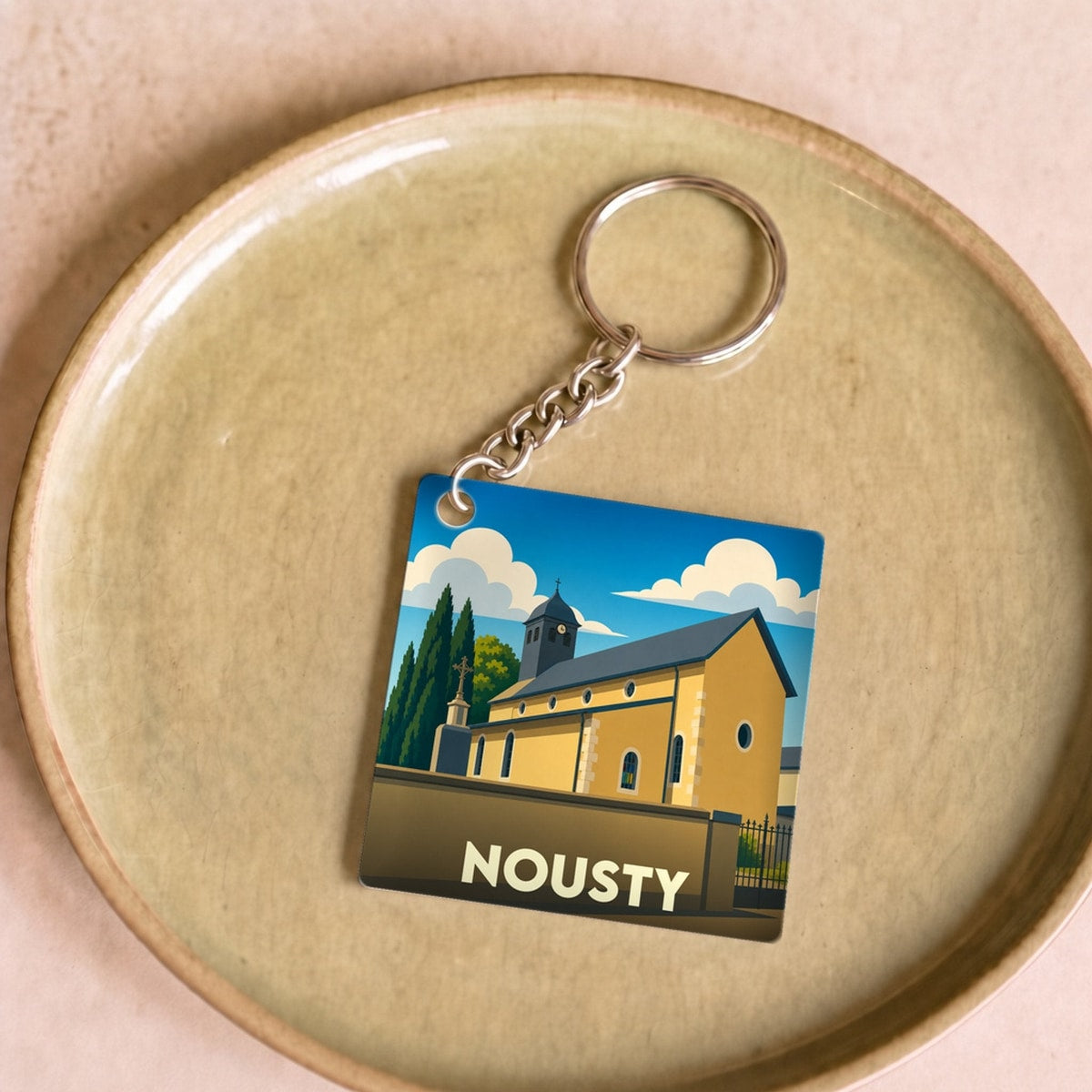 Porte-clés souvenir de la ville de Nousty avec une illustration stylisée de son église.