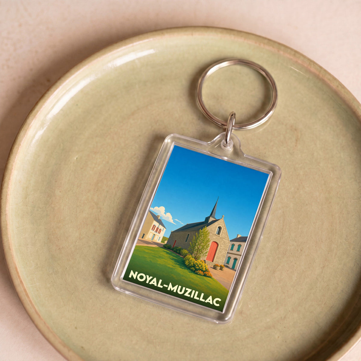 Porte-clés souvenir de la ville de Noyal-Muzillac avec une illustration stylisée d'une église sous un ciel bleu.