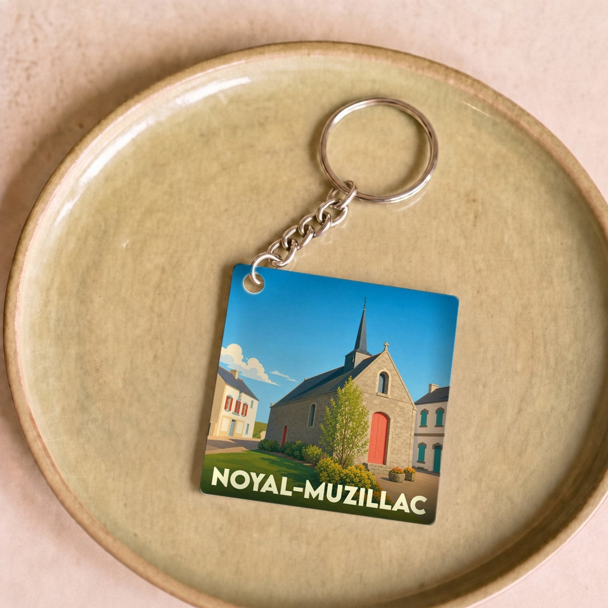 Porte-clés souvenir de la ville de Noyal-Muzillac avec une illustration stylisée d'une église sous un ciel bleu.