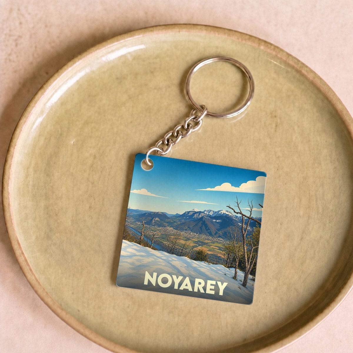 Porte-clés souvenir de la ville de Noyarey avec une illustration stylisée d'un paysage montagneux enneigé.