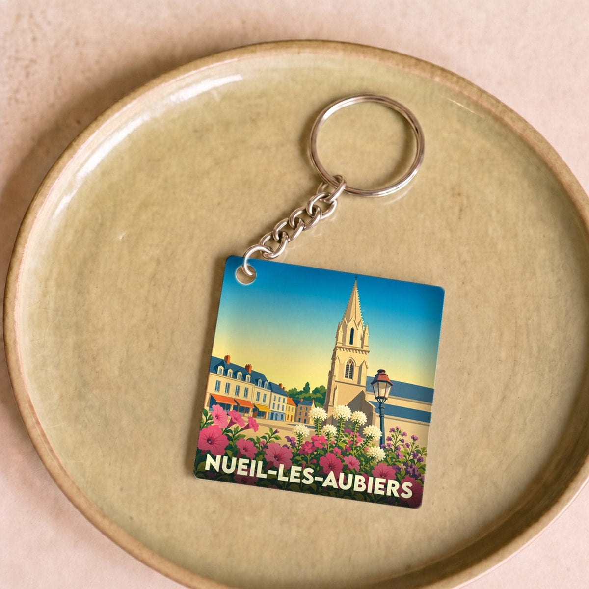 Porte-clés souvenir de la ville de Nueil-les-Aubiers avec une illustration stylisée et colorée.