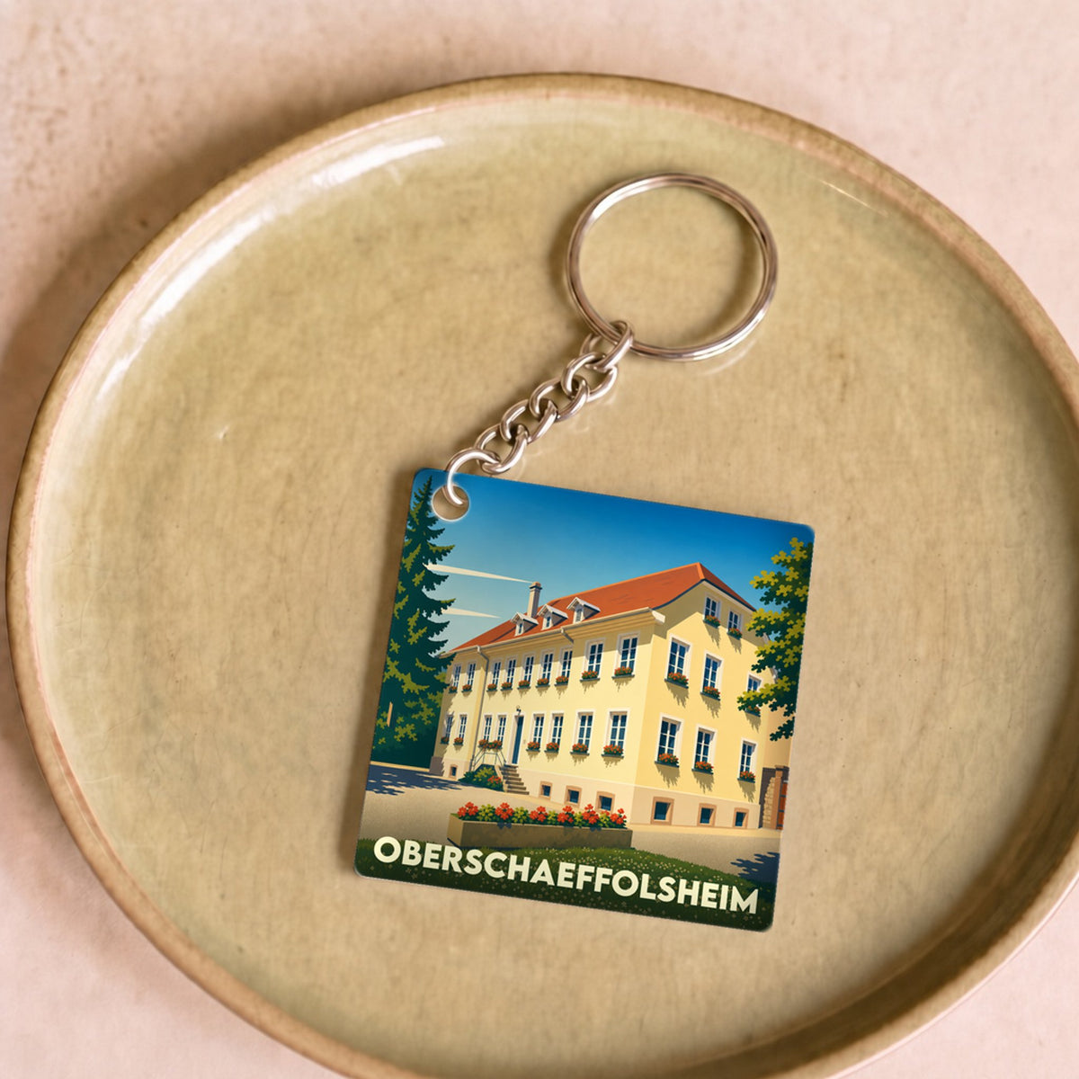 Porte-clés souvenir de la ville de Oberschaeffolsheim avec une illustration stylisée d'une maison traditionnelle.