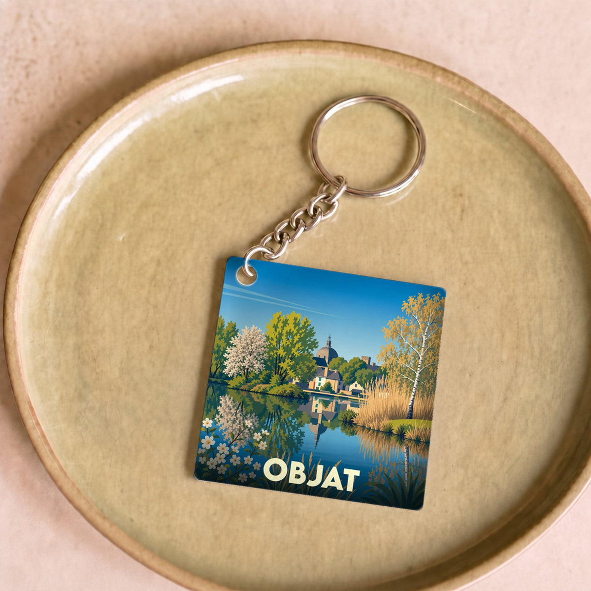 Porte-clés souvenir de la ville d'Objat avec une illustration stylisée d'un paysage lacustre.