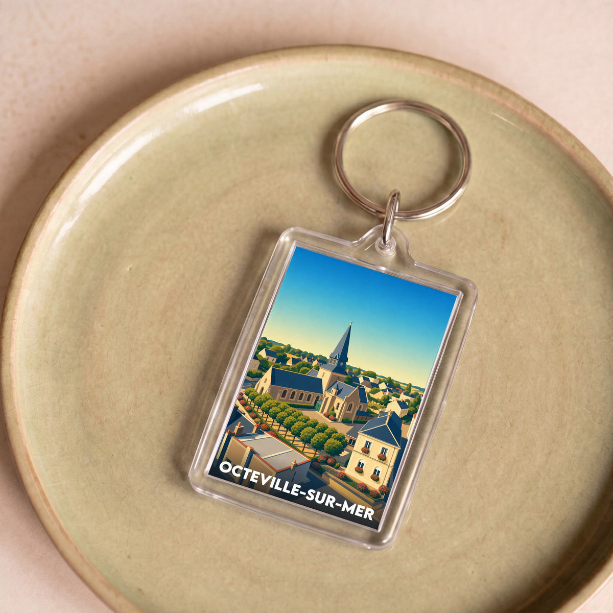 Porte-clés souvenir de la ville d'Octeville-sur-Mer avec une illustration stylisée de son église et de ses maisons.