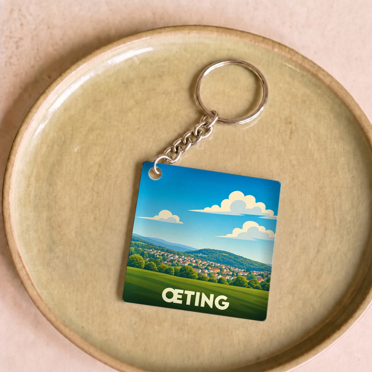 Porte-clés souvenir de la ville de Œting avec une illustration stylisée d'un paysage verdoyant.