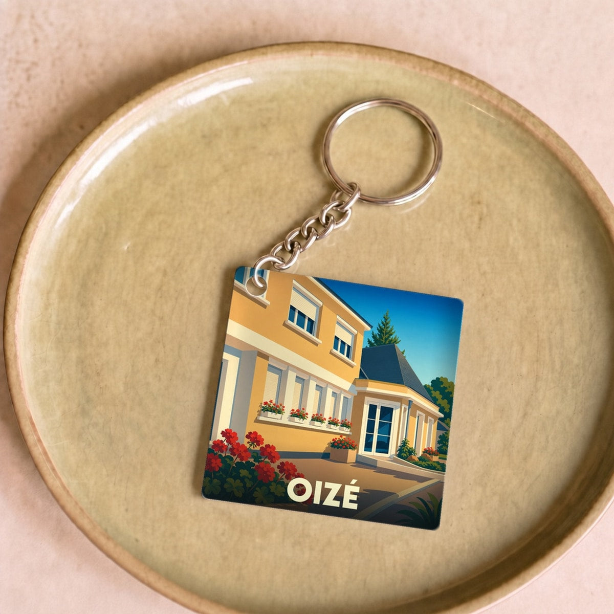 Porte-clés souvenir de la ville de Oizé avec une illustration stylisée d'une maison fleurie.