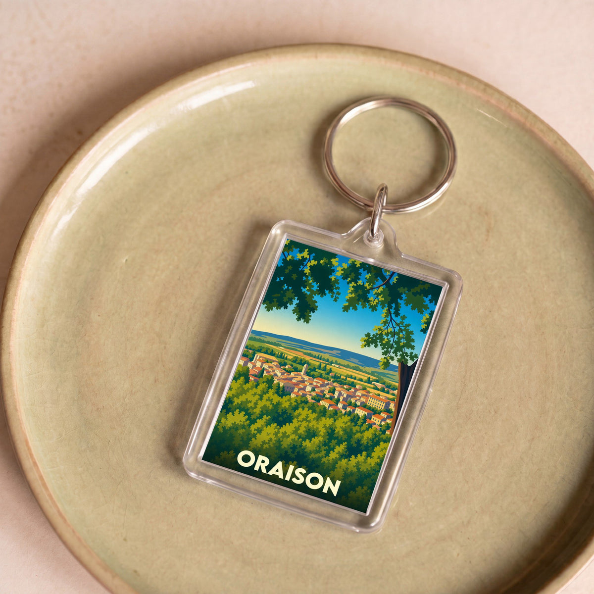 Porte-clés souvenir de la ville d'Oraison avec une illustration stylisée d'un paysage provençal.