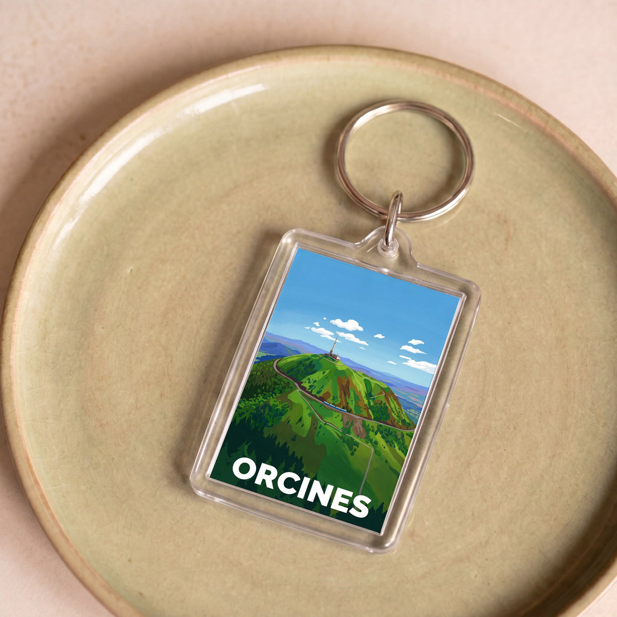 Porte-clés souvenir de la ville d'Orcines avec une illustration stylisée d'un paysage montagneux.