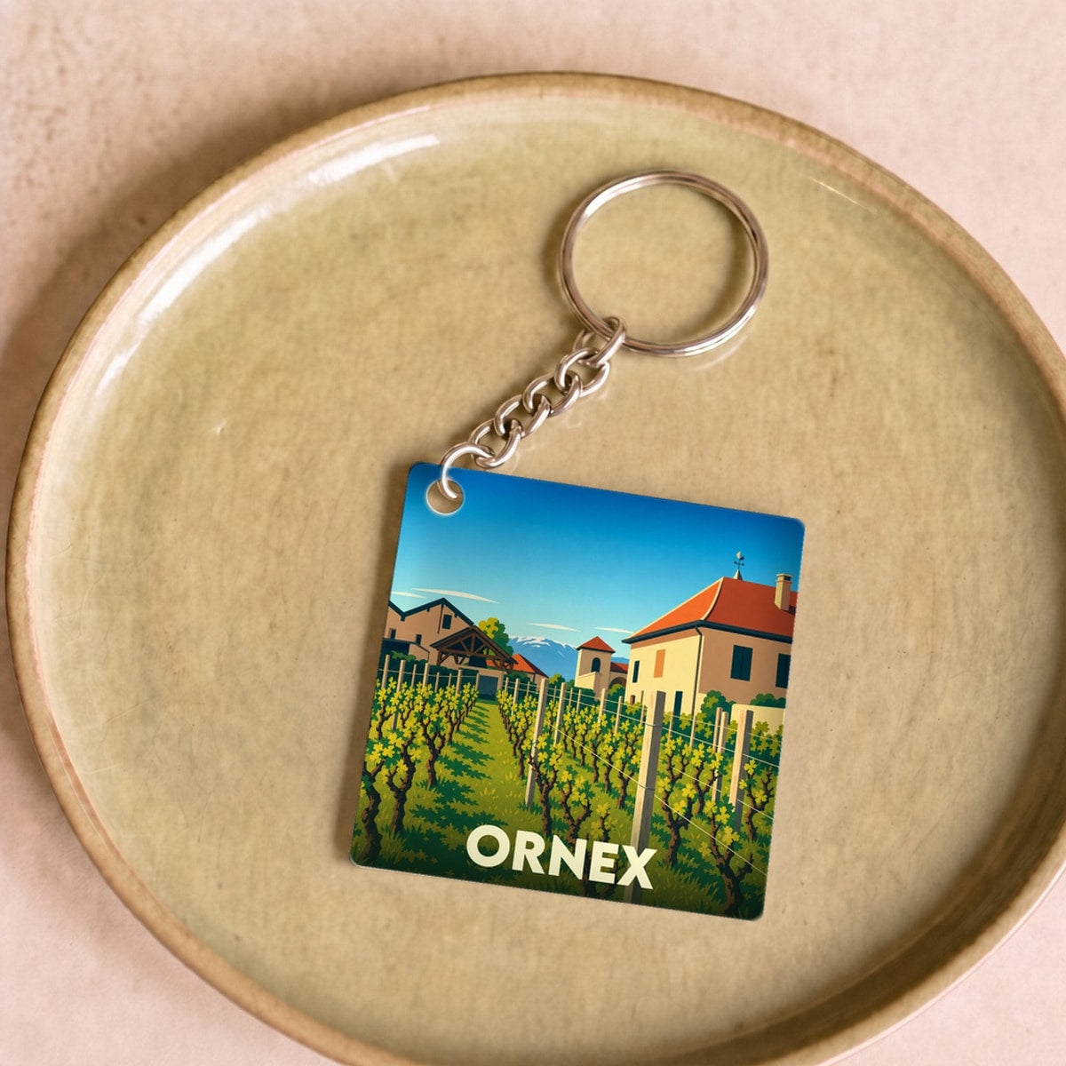 Porte-clés souvenir de la ville de Ornex avec une illustration stylisée d'un vignoble et de maisons typiques.