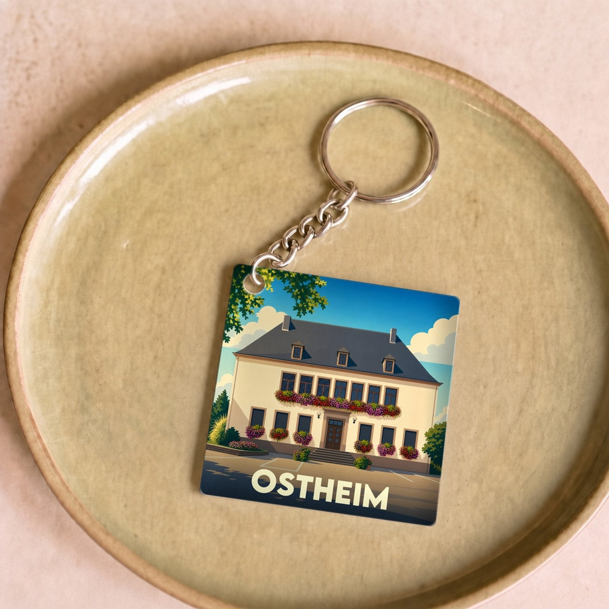 Porte-clés souvenir de la ville d'Ostheim avec une illustration stylisée d'un bâtiment fleuri.
