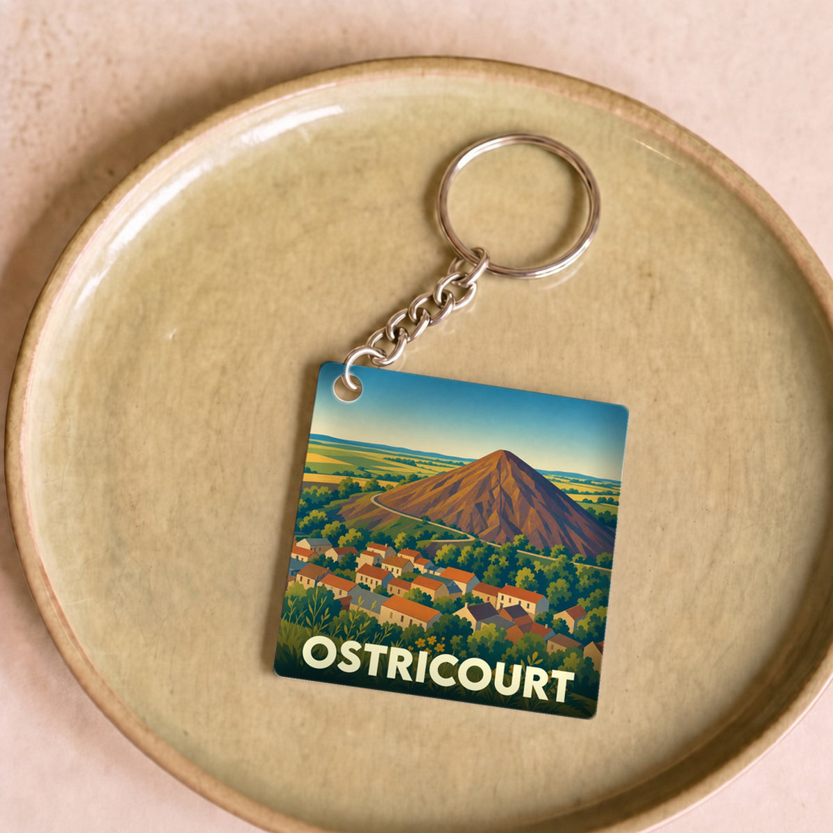 Porte-clés souvenir de la ville d'Ostricourt avec une illustration stylisée d'un terril dominant le village.