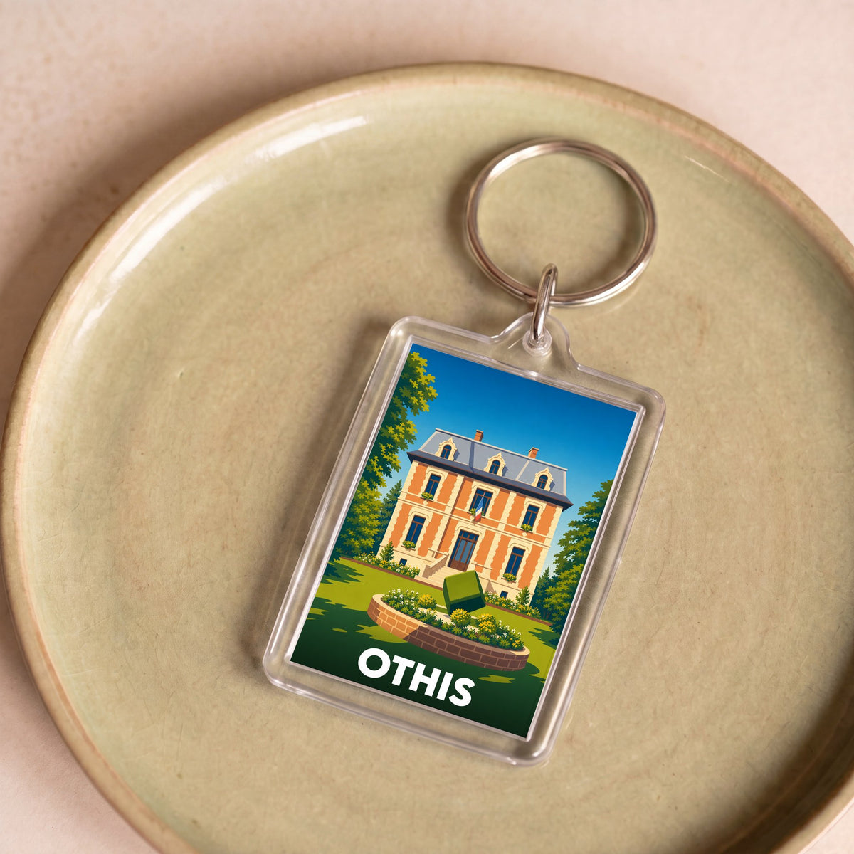 Porte-clés souvenir de la ville d'Othis avec une illustration stylisée d'une demeure bourgeoise.