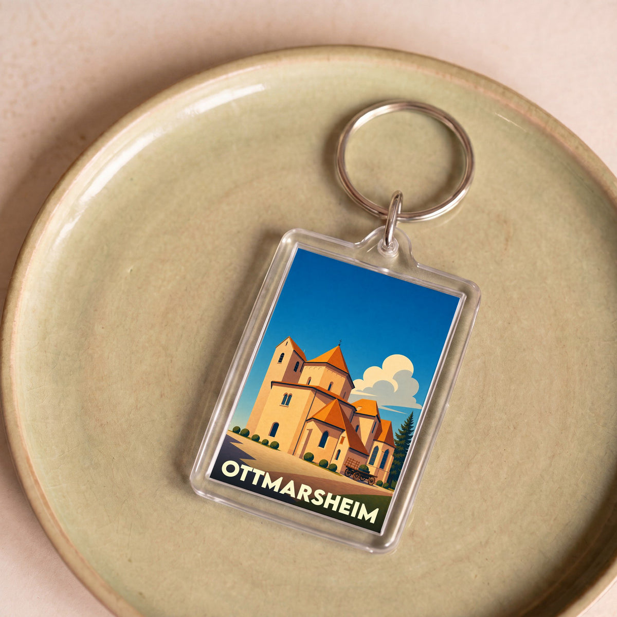 Porte-clés souvenir de la ville d'Ottmarsheim avec une illustration stylisée de son église abbatiale.
