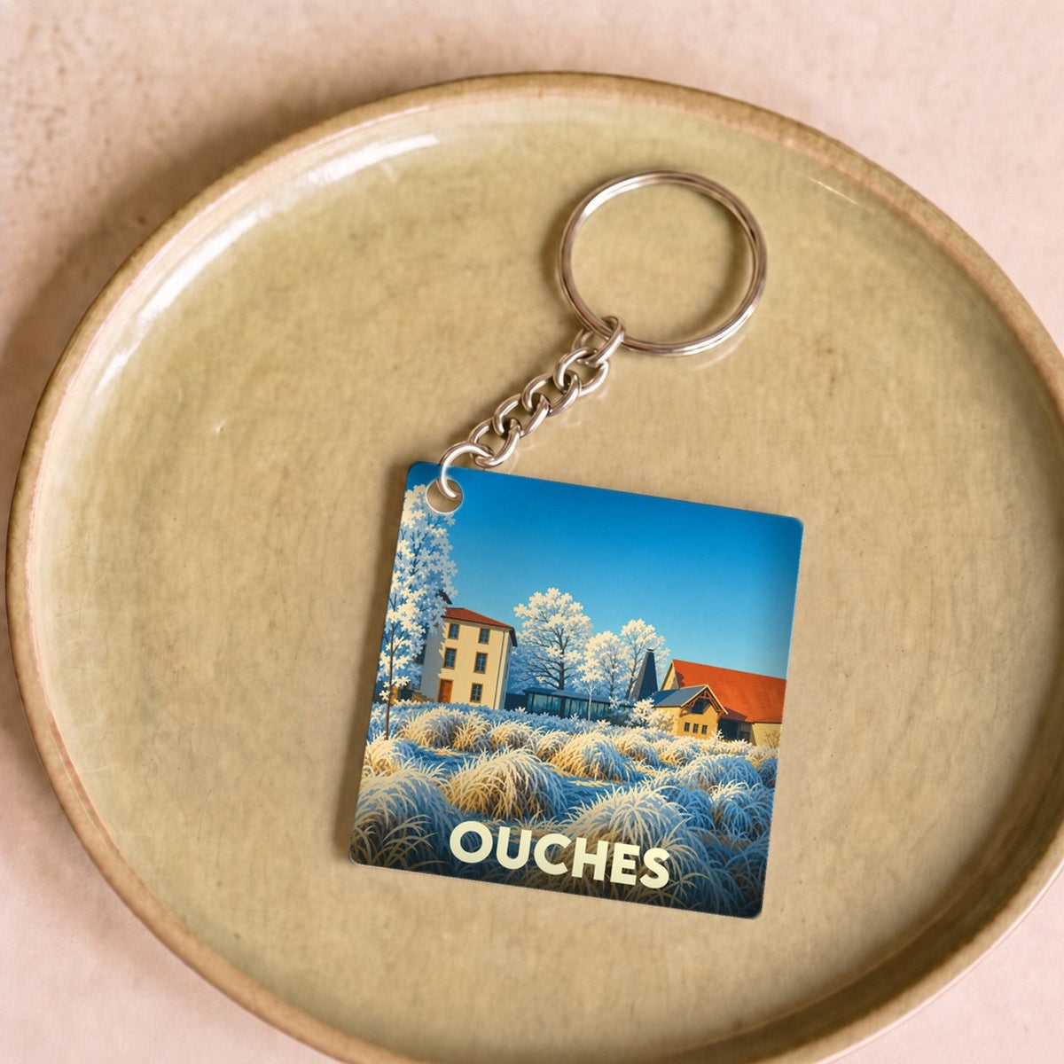 Porte-clés souvenir de la ville de Ouches avec une illustration stylisée de paysage.