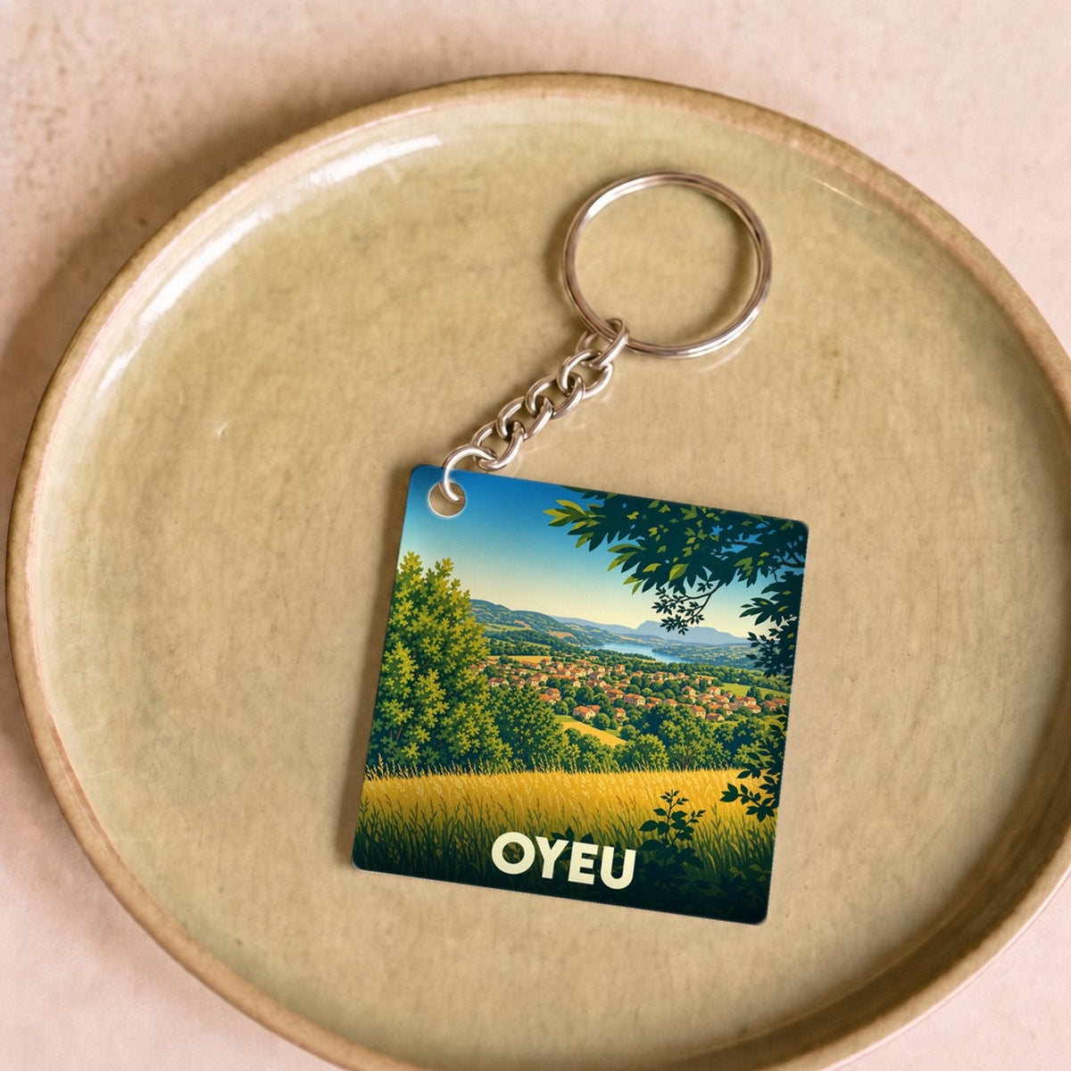 Porte-clés souvenir de la ville d'Oyeu avec une illustration stylisée d'un paysage champêtre.