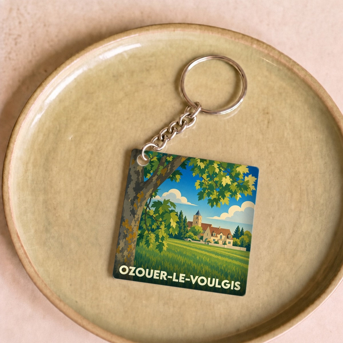 Porte-clés souvenir de la ville d'Ozouer-le-Voulgis avec une illustration de paysage champêtre.