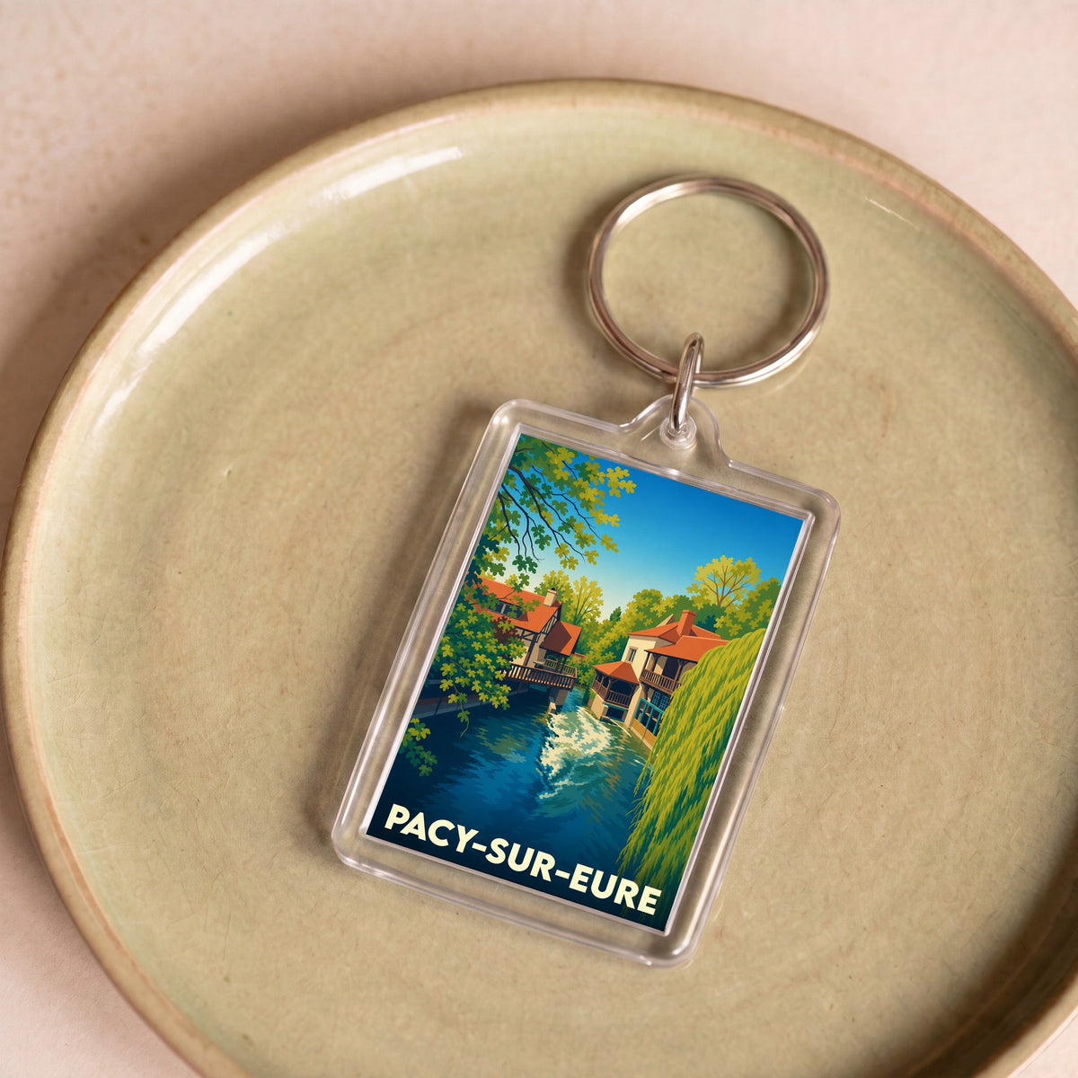 Porte-clés souvenir de la ville de Pacy-sur-Eure avec une illustration stylisée d'un paysage de rivière.
