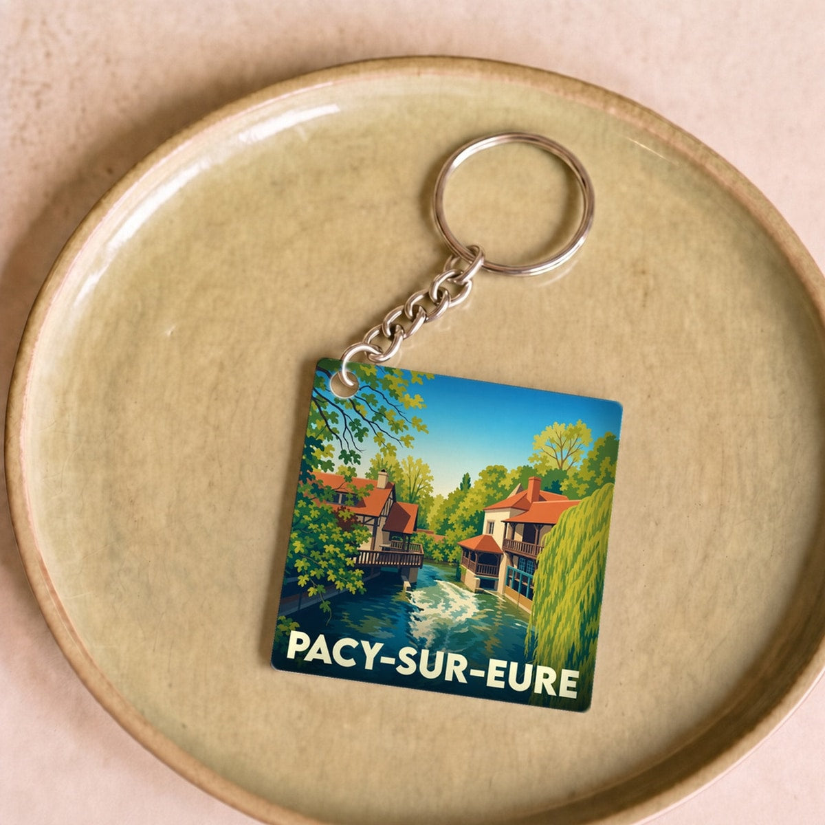 Porte-clés souvenir de la ville de Pacy-sur-Eure avec une illustration stylisée d'un paysage de rivière.