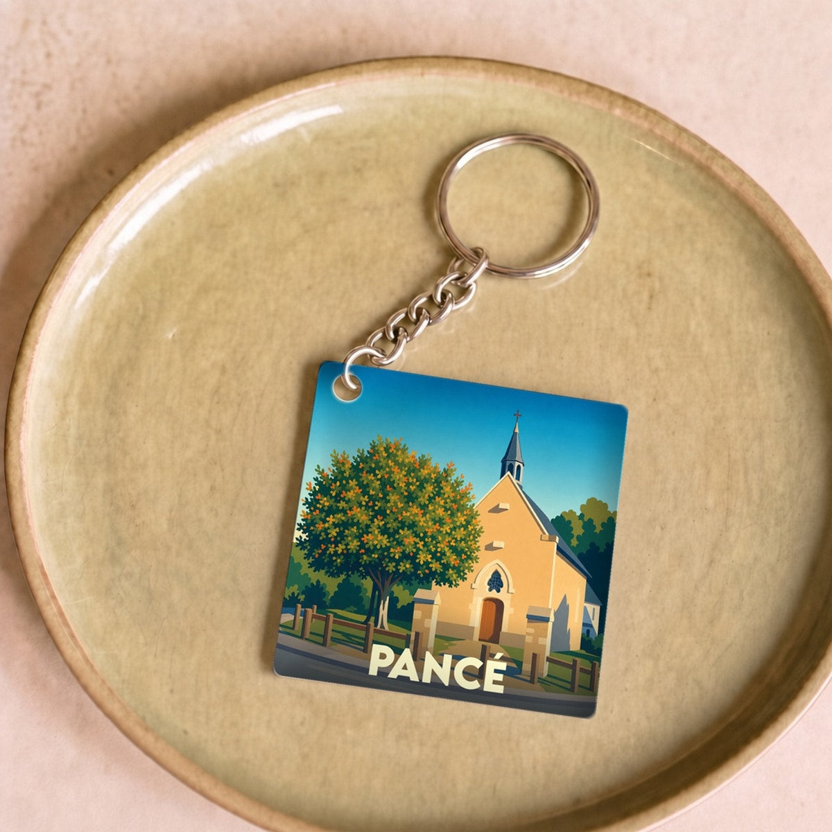 Porte-clés souvenir de la ville de Pancé avec une illustration stylisée d'une église sous un ciel bleu.