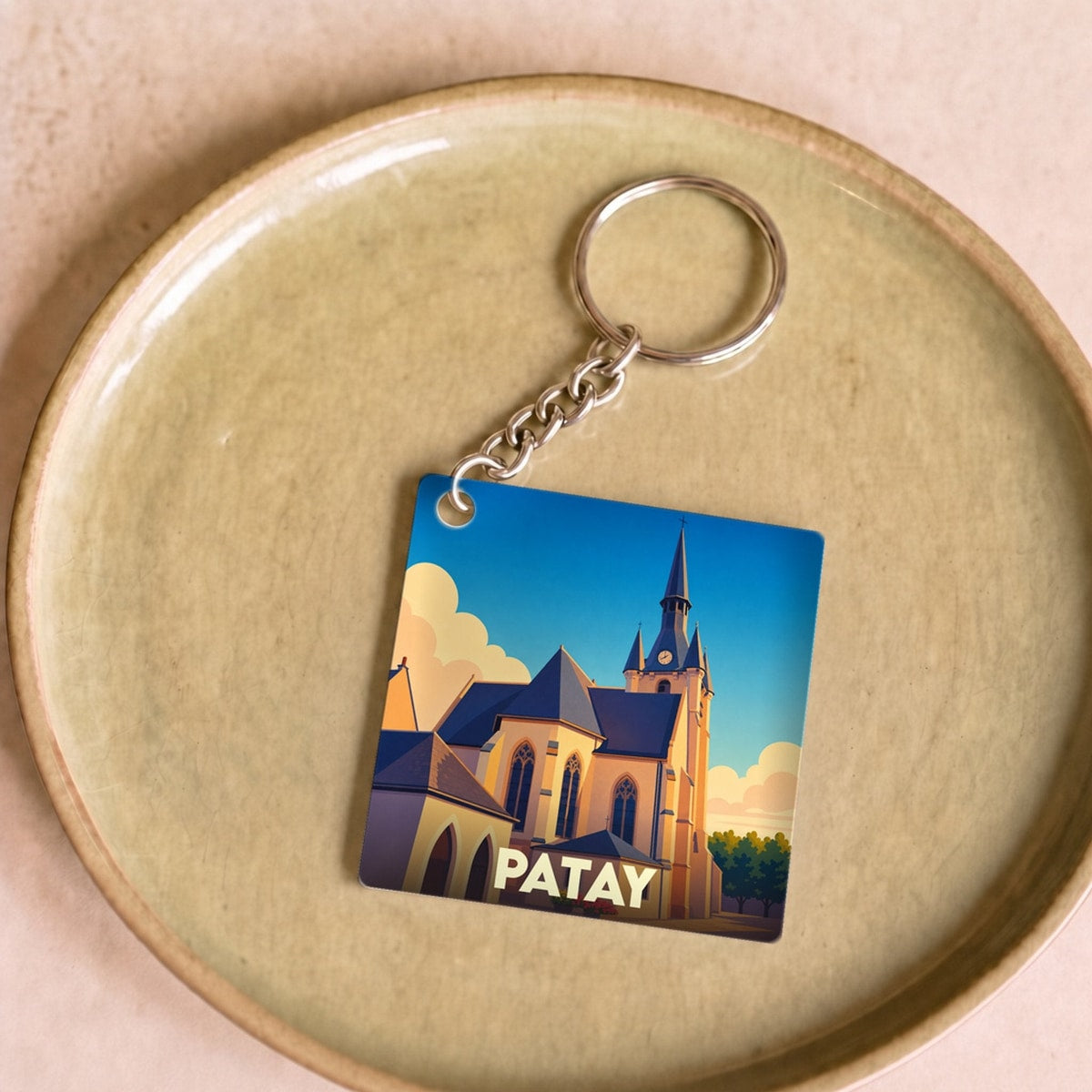 Porte-clés souvenir de la ville de Patay avec une illustration stylisée de son église sous un ciel bleu.