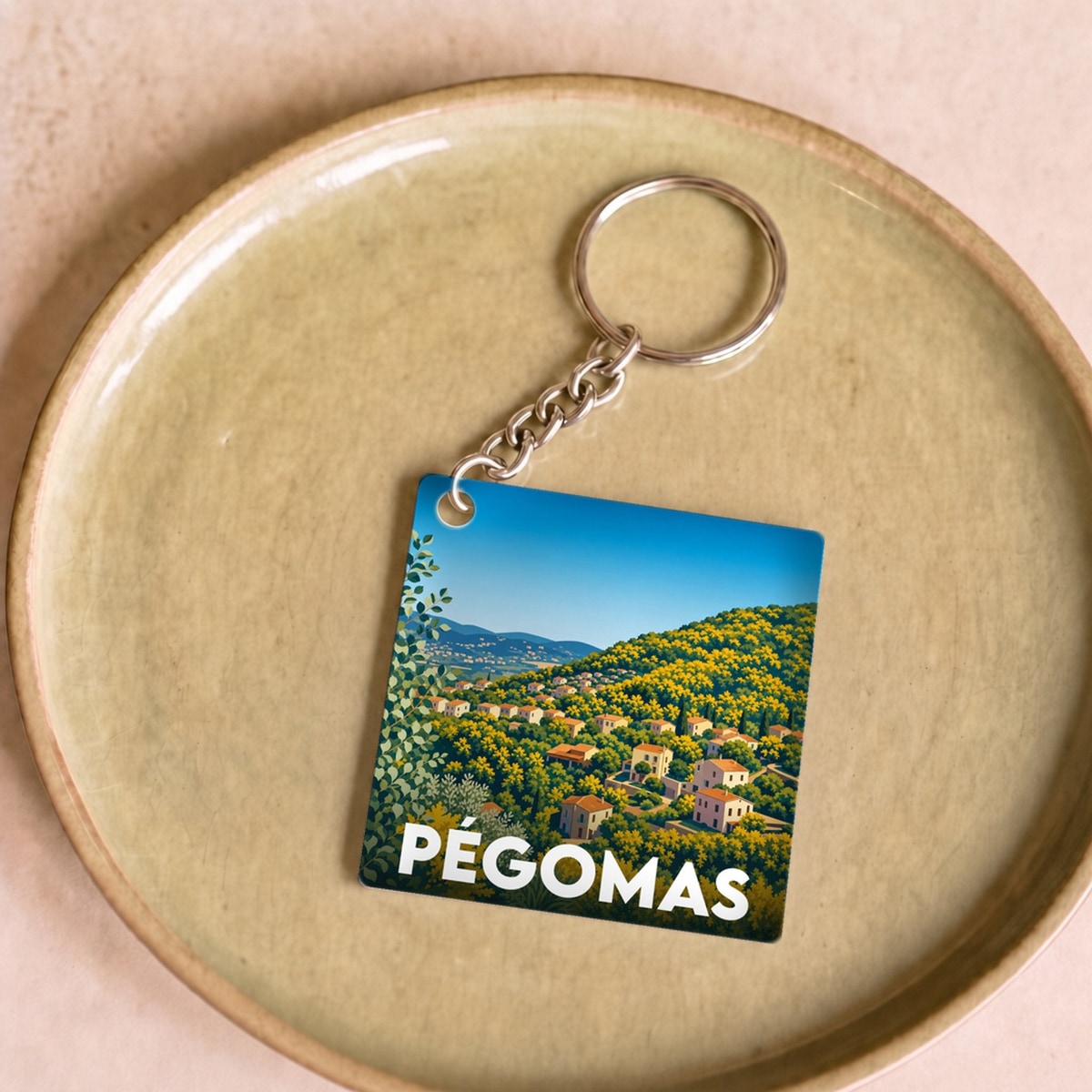 Porte-clés souvenir de la ville de Pégomas avec une illustration stylisée de son paysage vallonné.
