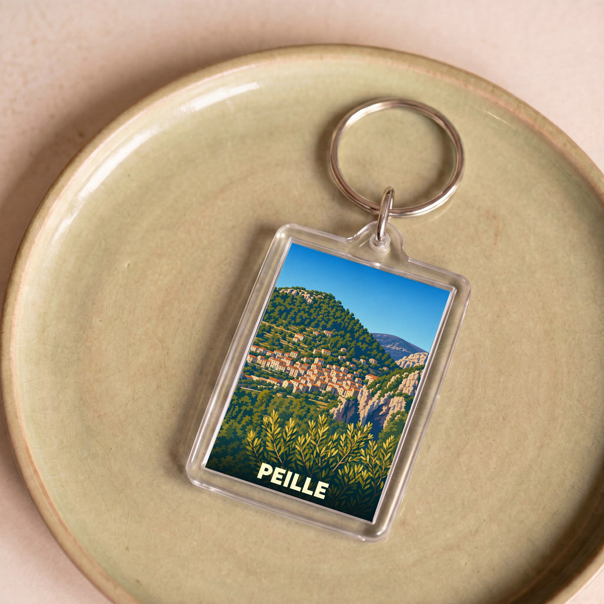 Porte-clés souvenir de la ville de Peille avec une illustration stylisée de son village perché.