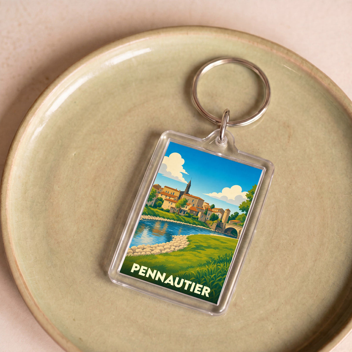 Porte-clés souvenir de la ville de Pennautier avec une illustration stylisée d'un paysage urbain au bord de l'eau.