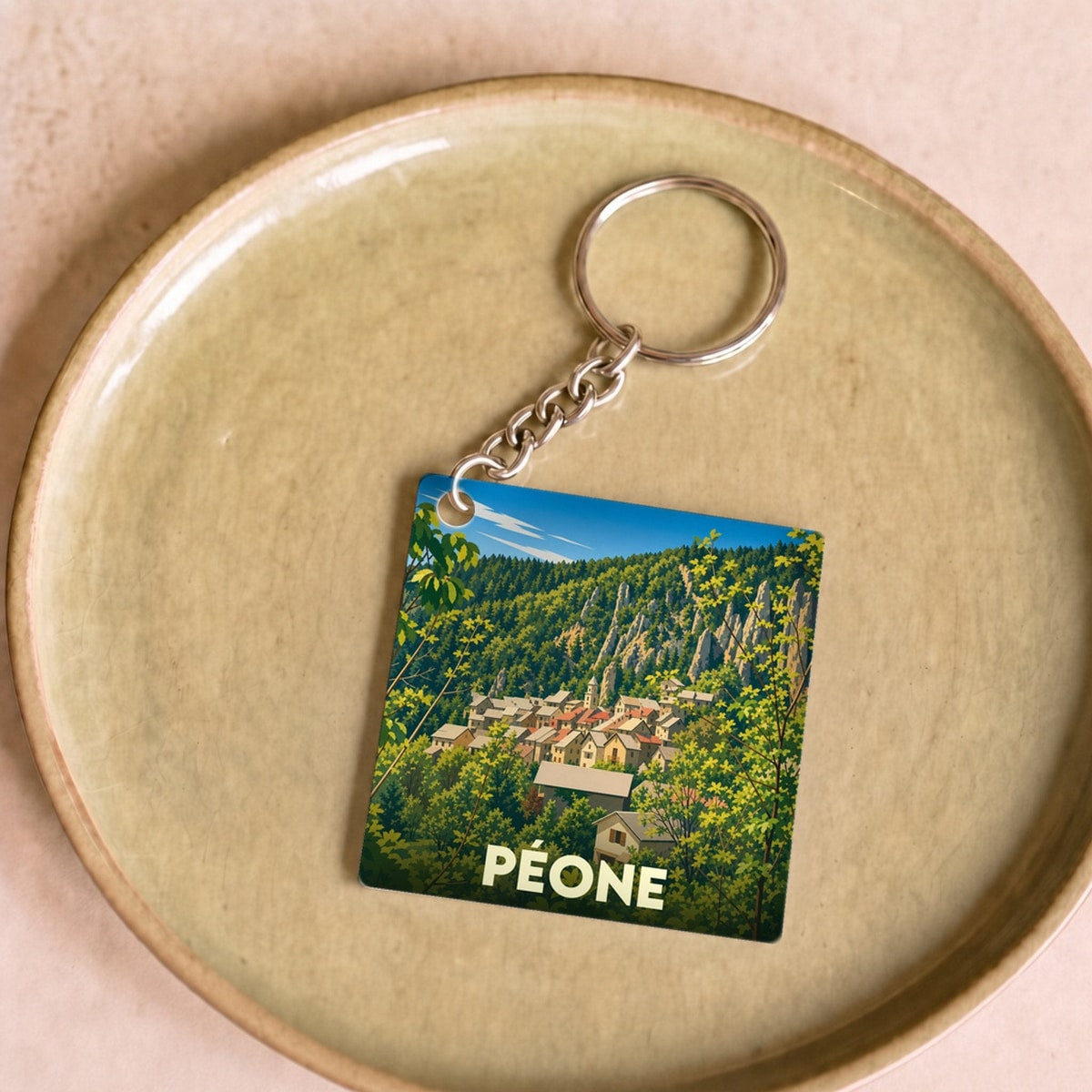 Porte-clés souvenir de la ville de Péone avec une illustration stylisée de son village niché dans la montagne.
