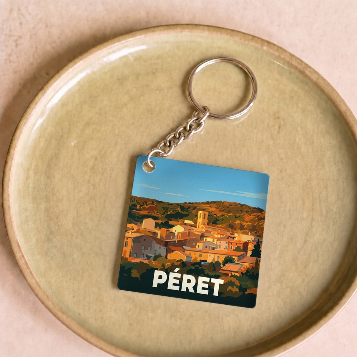 Porte-clés souvenir de la ville de Péret avec une illustration stylisée.
