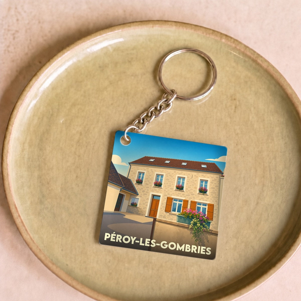 Porte-clés souvenir de la ville de Péroy-les-Gombries avec une illustration stylisée d'une maison fleurie.