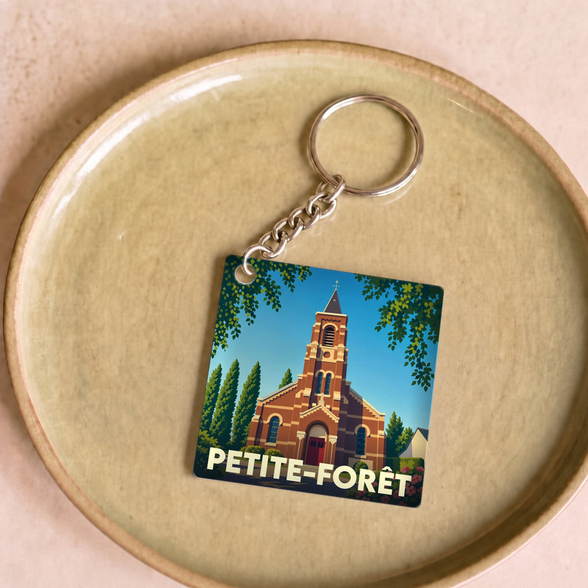 Porte-clés souvenir de la ville de Petite-Forêt avec une illustration stylisée de son église.