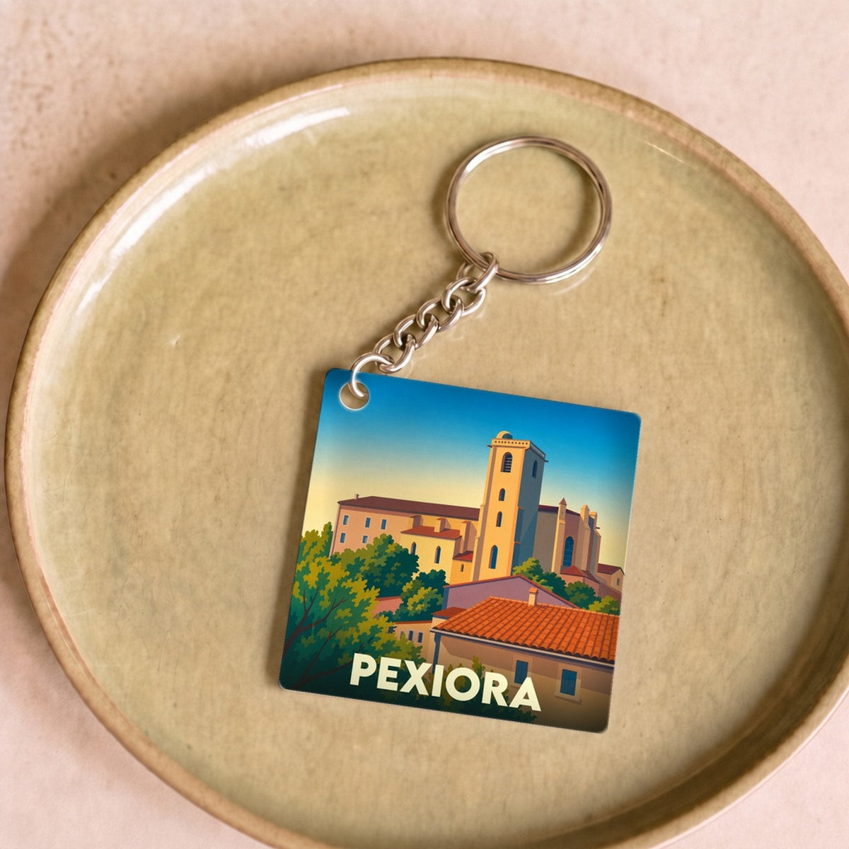 Porte-clés souvenir de la ville de Pexiora avec une illustration stylisée de son église et de ses toits.