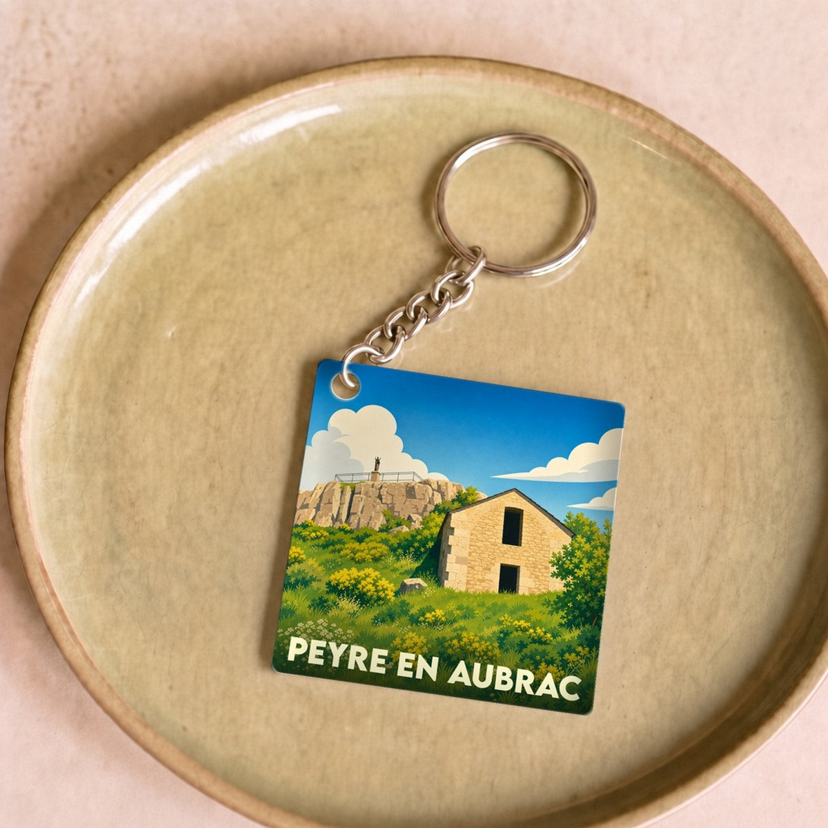 Porte-clés souvenir de la ville de Peyre en Aubrac avec une illustration stylisée d'un paysage local.