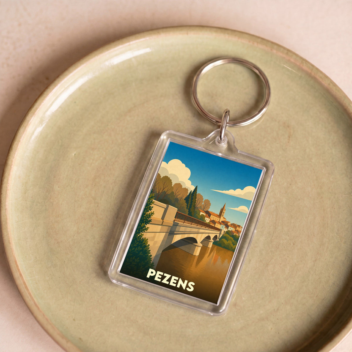 Porte-clés souvenir de la ville de Pezens avec une illustration stylisée d'un pont enjambant une rivière.