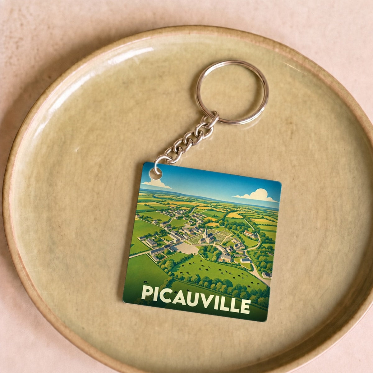 Porte-clés souvenir de la ville de Picauville avec une illustration stylisée de son paysage rural.