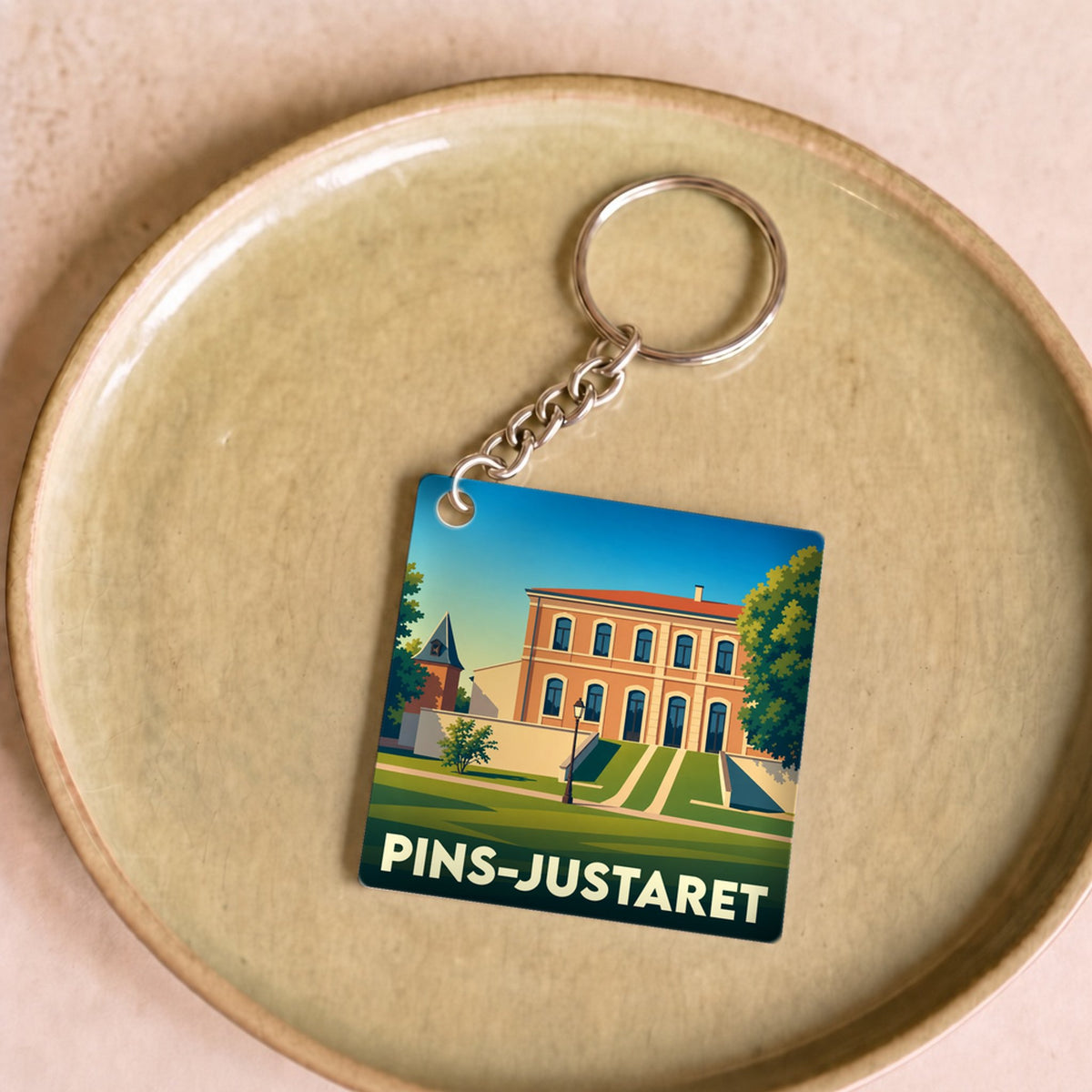 Porte-clés souvenir de la ville de Pins-Justaret avec une illustration stylisée.