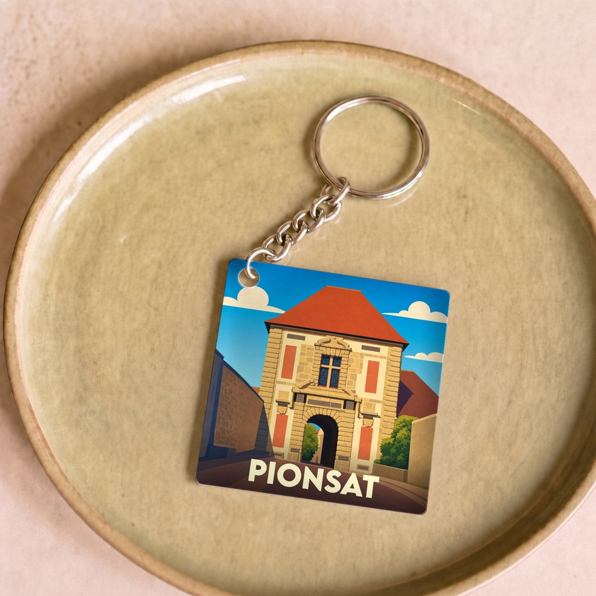 Porte-clés souvenir de la ville de Pionsat avec une illustration stylisée de son patrimoine.