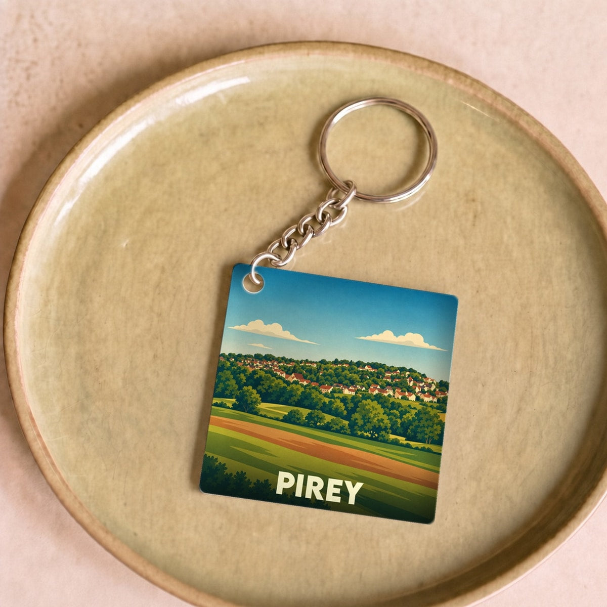 Porte-clés souvenir de la ville de Pirey avec une illustration stylisée de son paysage vallonné.