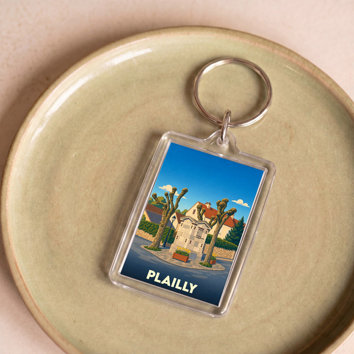 Porte-clés souvenir de la ville de Plailly avec une illustration stylisée d'une fontaine et de platanes.