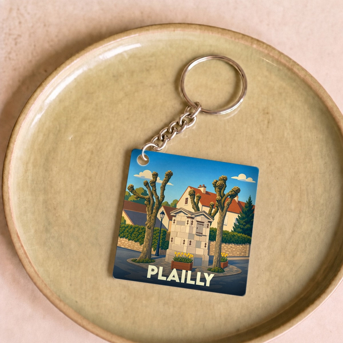 Porte-clés souvenir de la ville de Plailly avec une illustration stylisée d'une fontaine et de platanes.