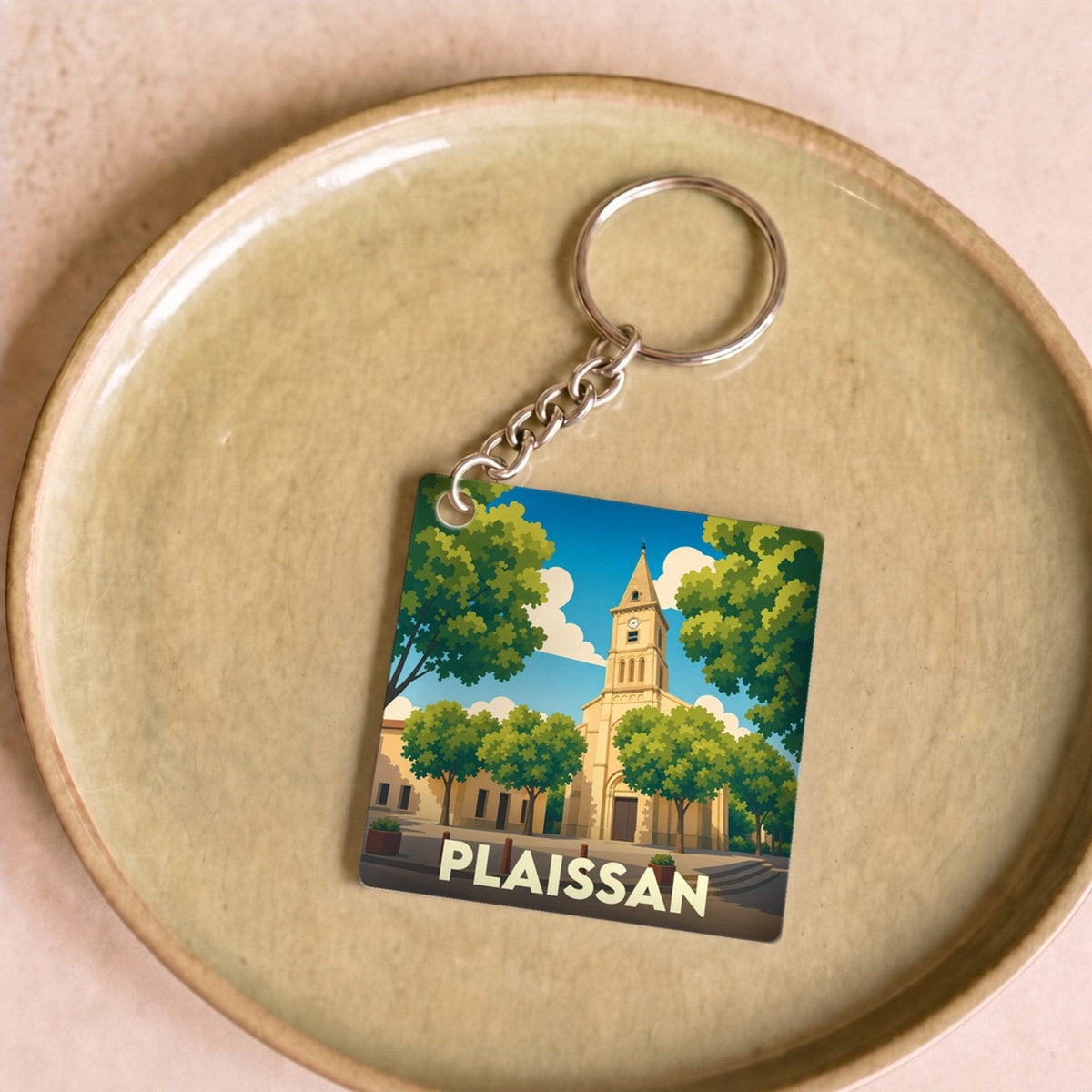 Porte-clés souvenir de la ville de Plaissan avec une illustration stylisée de son église entourée d'arbres.