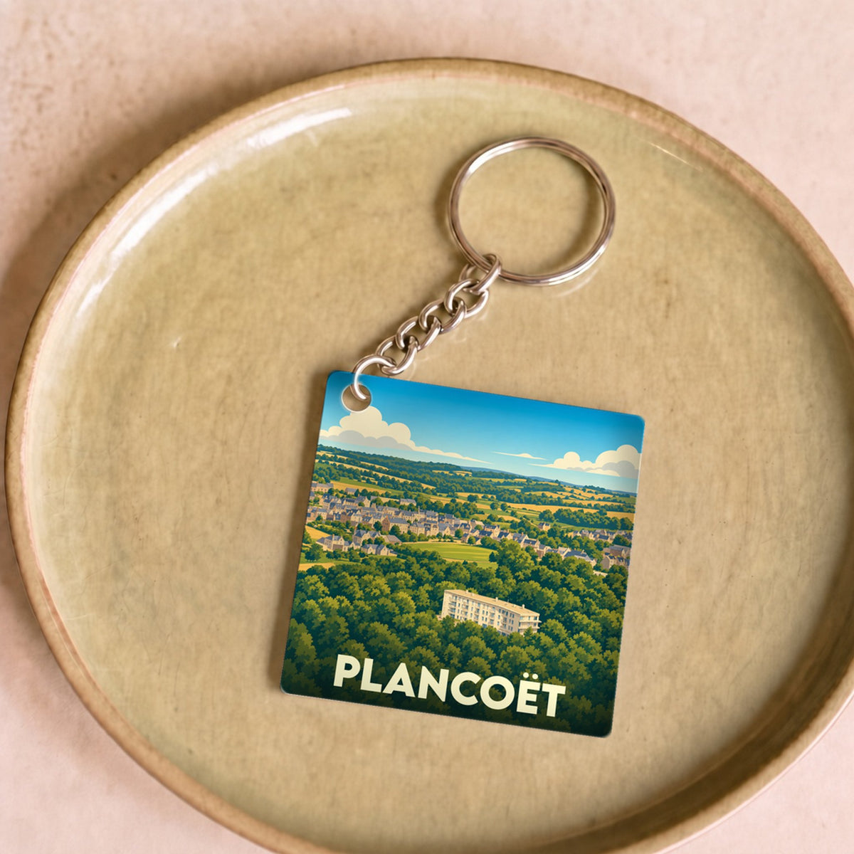 Porte-clés souvenir de la ville de Plancoët avec une illustration stylisée de son paysage verdoyant.
