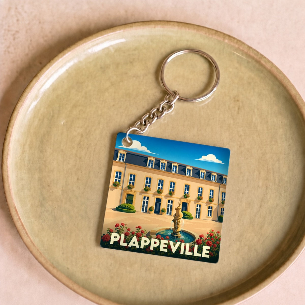 Porte-clés souvenir de la ville de Plappeville avec une illustration stylisée d'une demeure historique et sa fontaine.