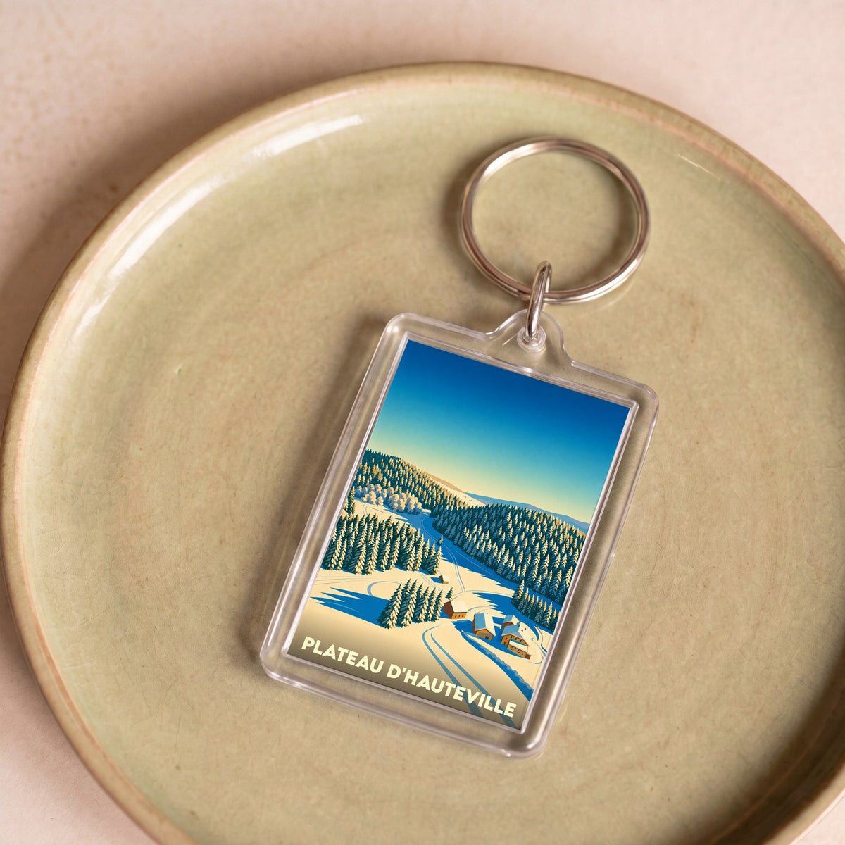 Porte-clés souvenir de Plateau d'Hauteville avec une illustration stylisée d'un paysage de montagne enneigé.