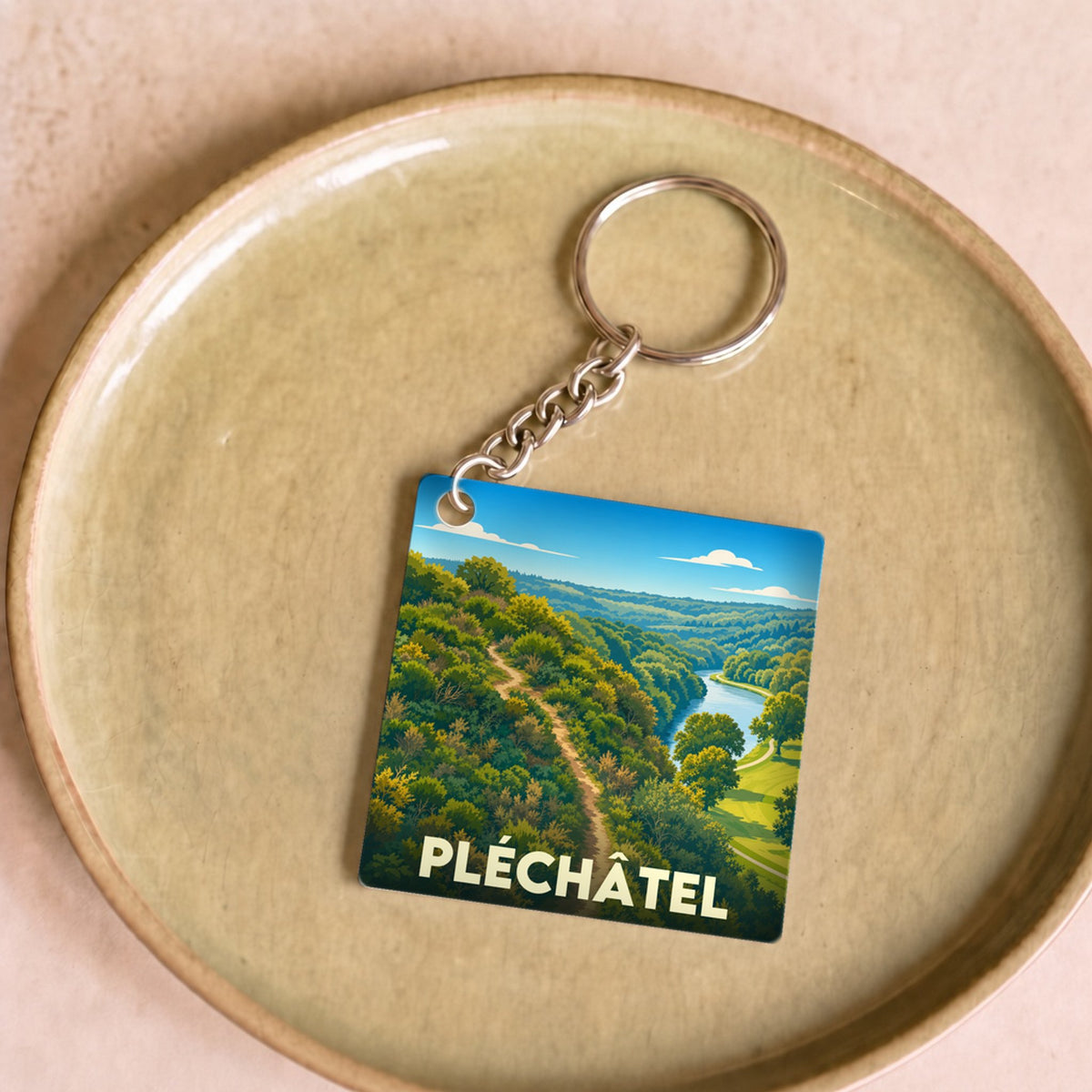 Porte-clés souvenir de la ville de Pléchâtel avec une illustration stylisée de son paysage naturel.