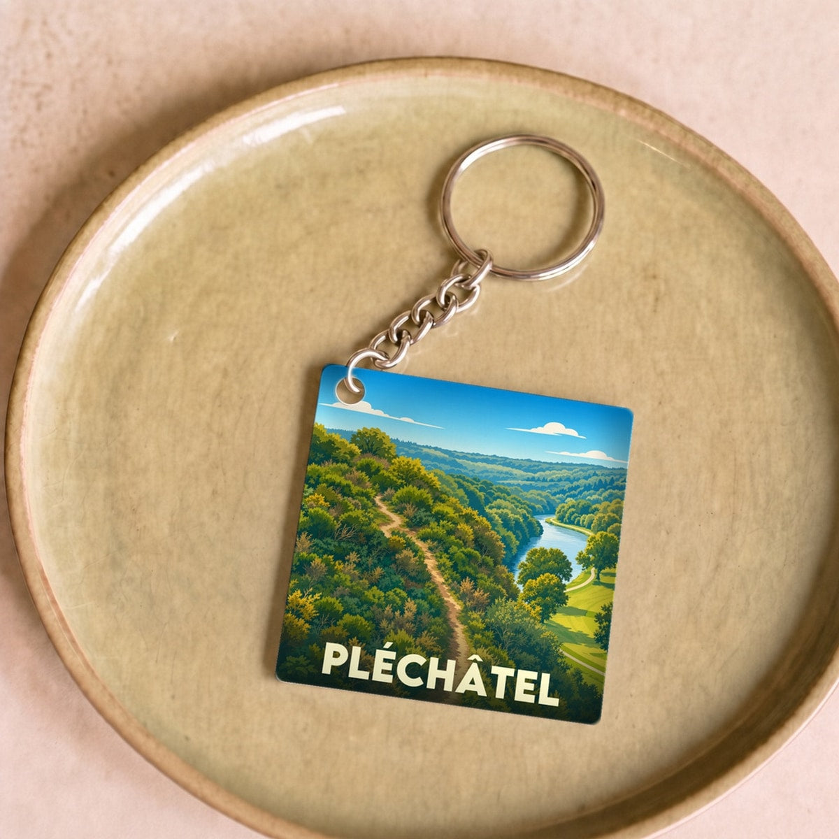 Porte-clés souvenir de la ville de Pléchâtel avec une illustration stylisée de son paysage naturel.